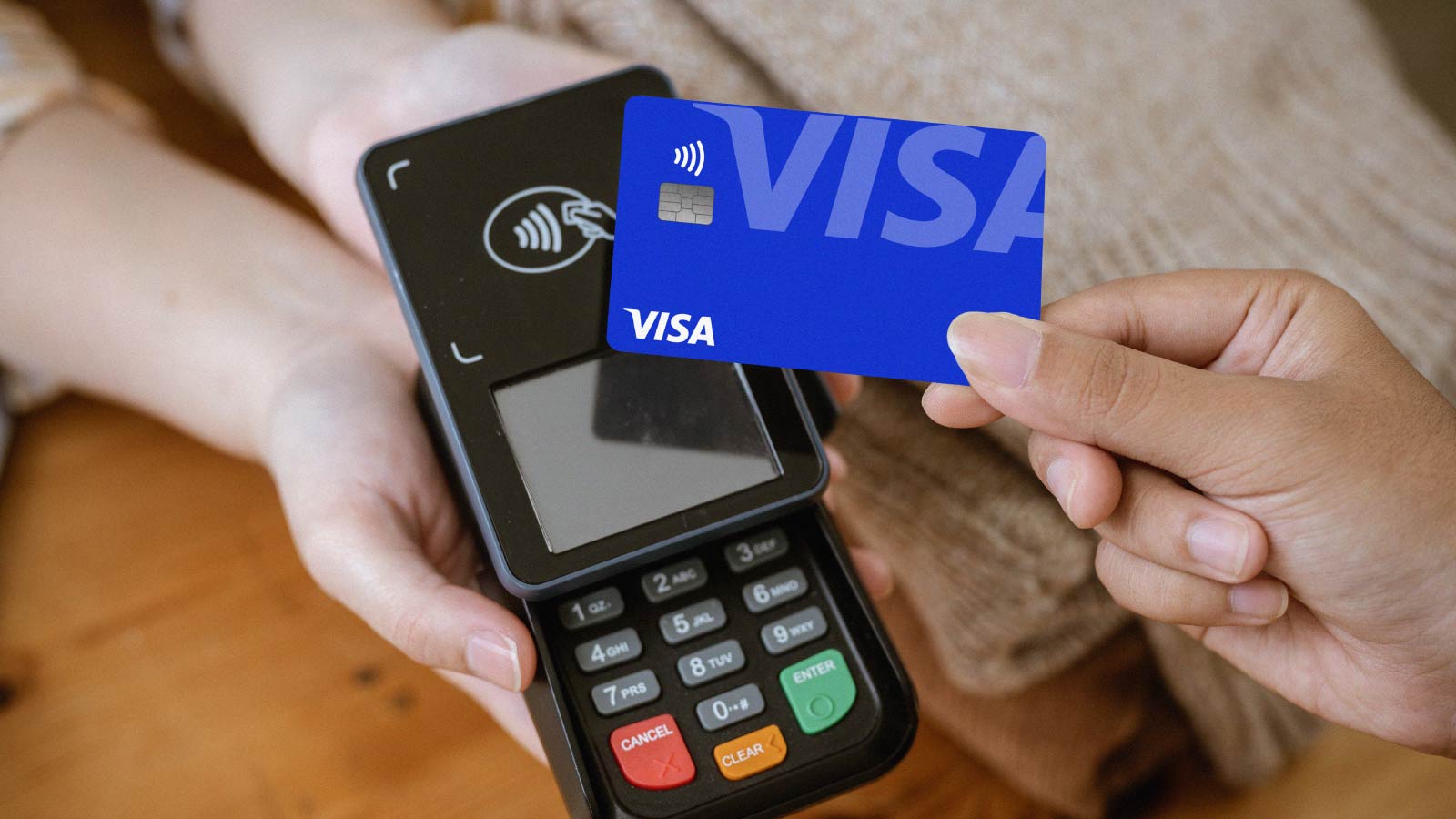 A close-up image of a customer tapping her Visa card with a payment terminal in a clothing store. 