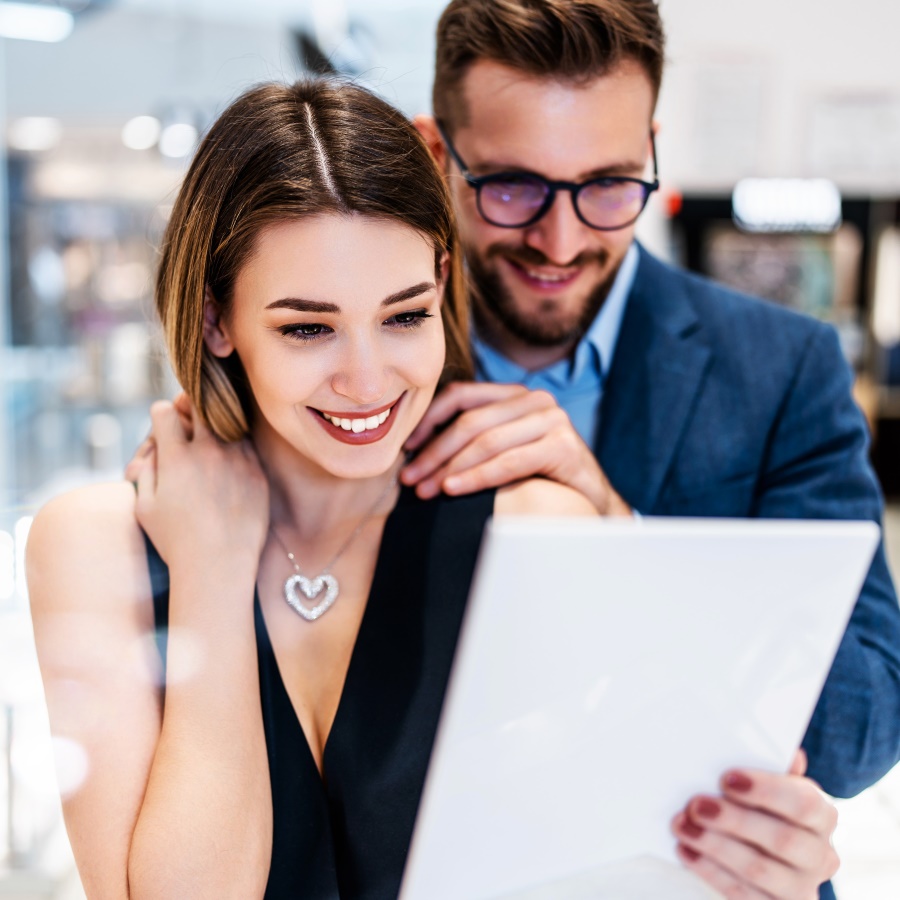 A man helping woman to try on a piece of jewellery in a shop