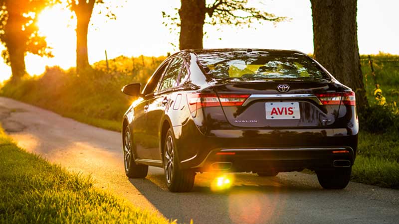 Avis rental car driving on country road at sunset.