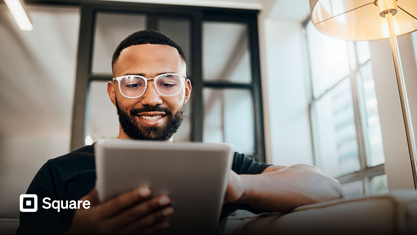 Man using tablet at home with Square logo in corner of image.