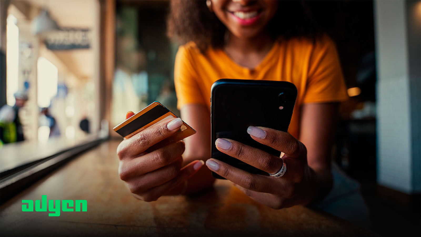 Woman paying by credit card on mobile phone with Adyen logo in corner of image.
